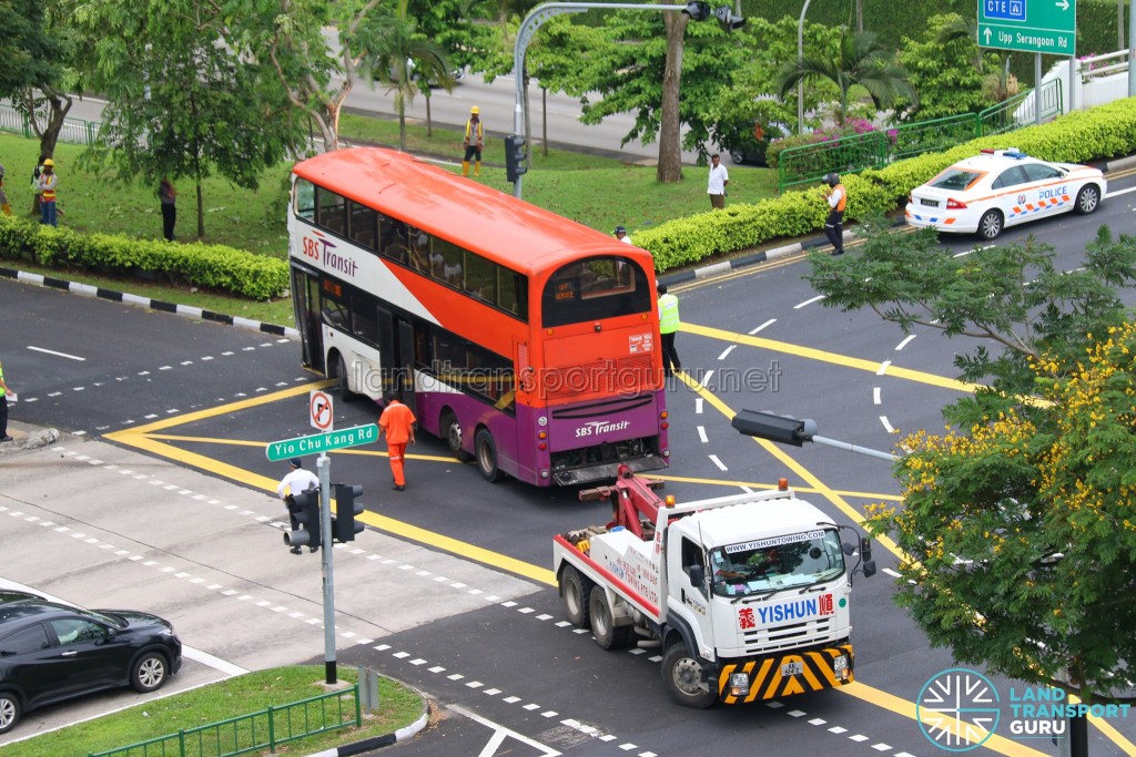The bus slowly reverses back onto the road with the assistance of the tow truck